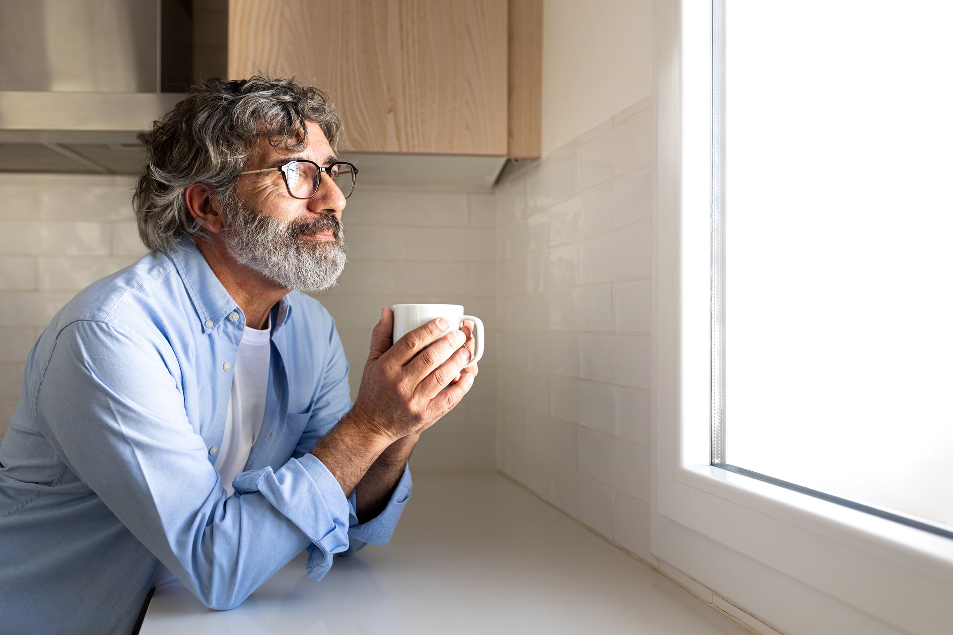 Happy mature man relaxing at home having morning coffee looking out the kitchen window. Copy space.