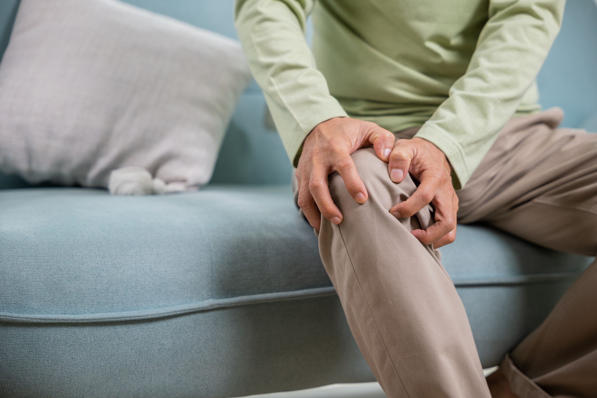 Asian senior man retirement knee joint pain on sofa